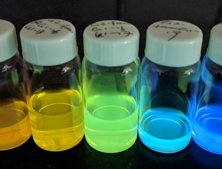a set of vials containing a rainbow of carbon dots glowing with bright colors